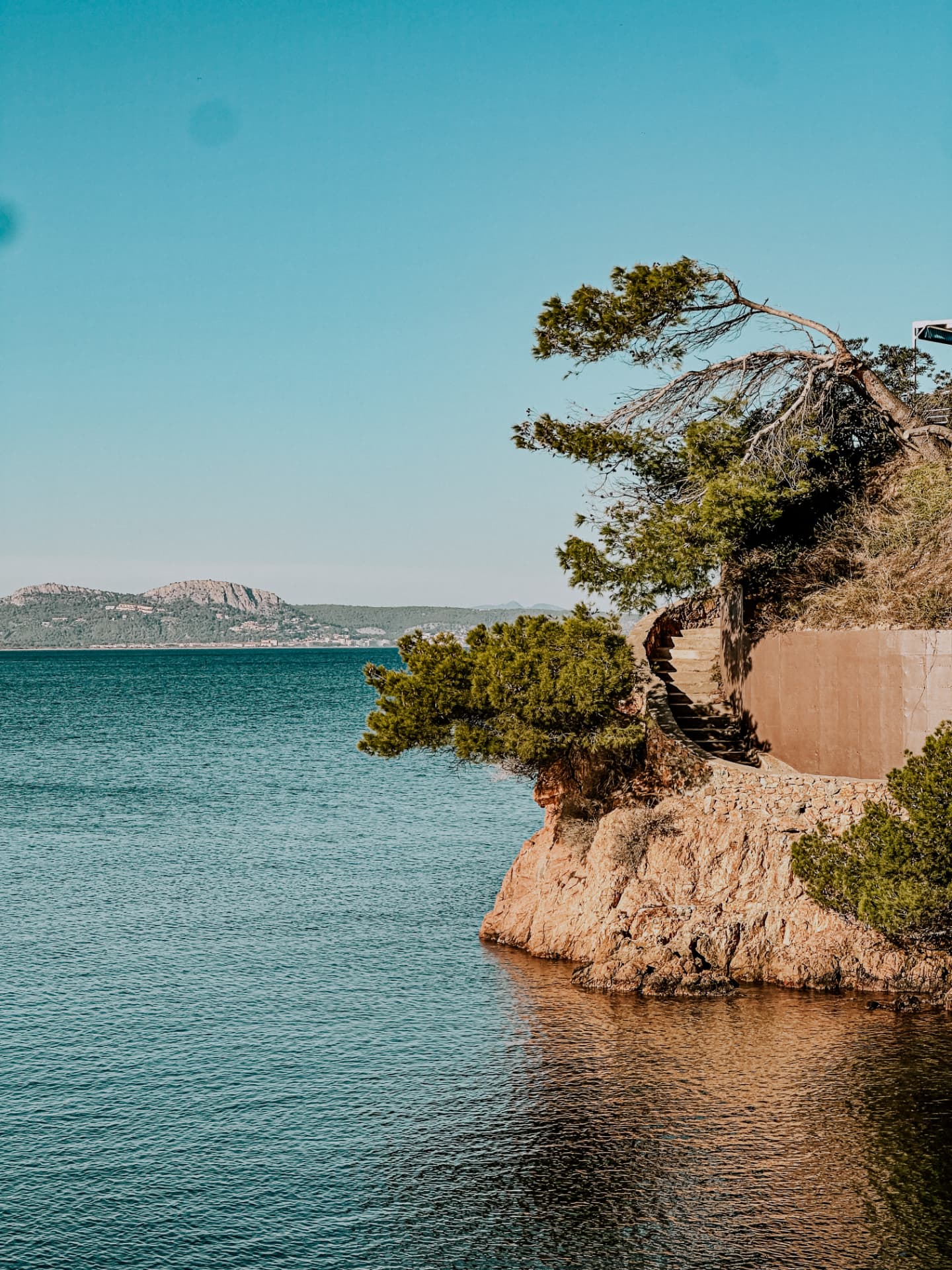 A stone stairway winding down a rocky cliff to a turquoise cove on the Costa Brava